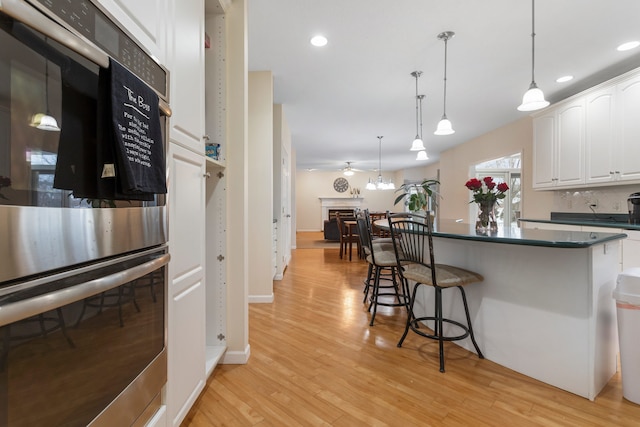 kitchen with ceiling fan, multiple ovens, light hardwood / wood-style flooring, pendant lighting, and white cabinets