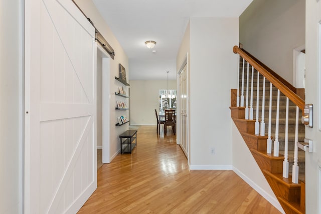 corridor featuring a chandelier, a barn door, and light hardwood / wood-style flooring