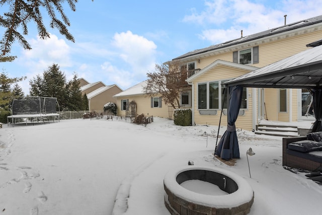 snow covered back of property with a trampoline and an outdoor fire pit