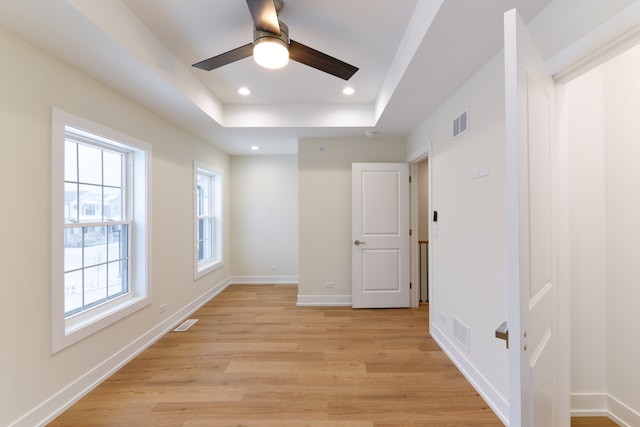 empty room with a raised ceiling, ceiling fan, and light hardwood / wood-style flooring