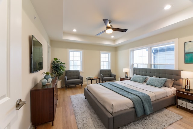 bedroom with a raised ceiling, light hardwood / wood-style flooring, and ceiling fan