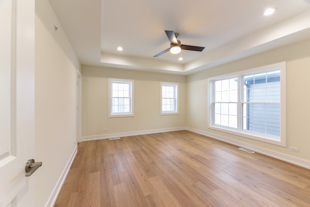 empty room with ceiling fan, a raised ceiling, and light wood-type flooring