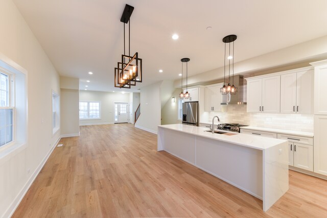 kitchen with stainless steel fridge, white cabinets, hanging light fixtures, and wall chimney range hood