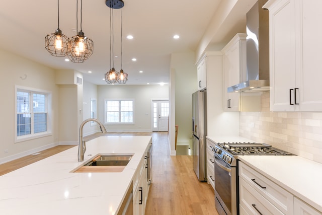 kitchen featuring a wealth of natural light, white cabinetry, wall chimney range hood, and appliances with stainless steel finishes