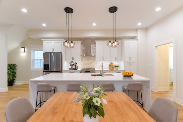 kitchen with sink, stainless steel appliances, a kitchen island with sink, and wall chimney range hood