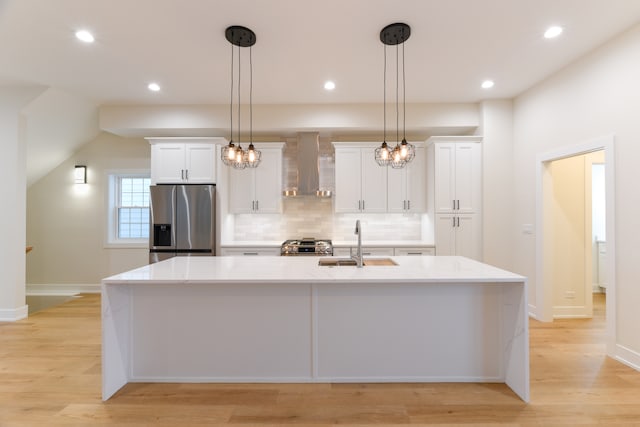 kitchen featuring stainless steel appliances, sink, wall chimney range hood, white cabinetry, and an island with sink