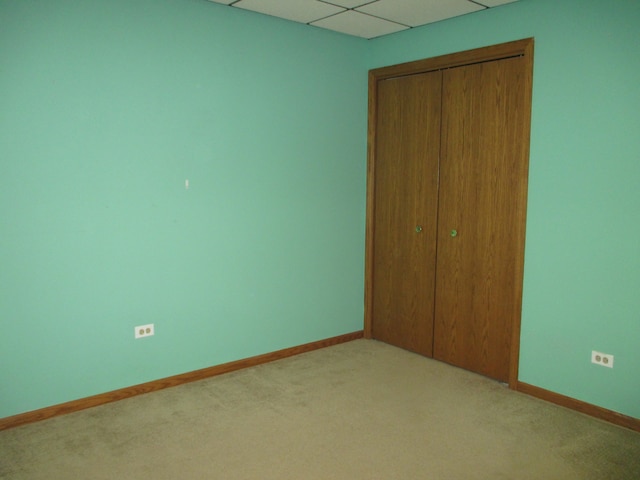 unfurnished bedroom featuring a paneled ceiling, a closet, and light colored carpet