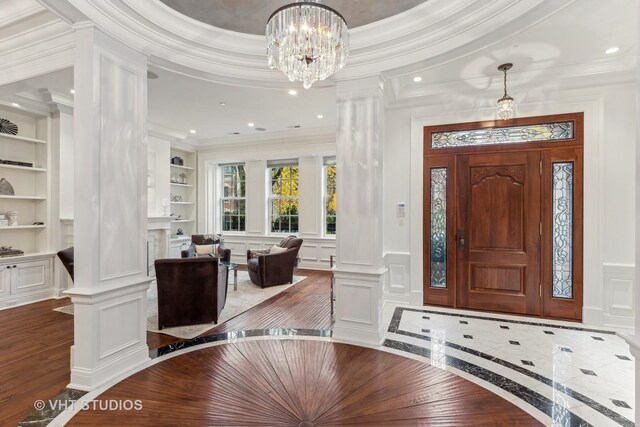 foyer featuring hardwood / wood-style floors, a chandelier, crown molding, and decorative columns