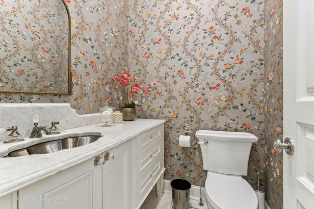 bathroom with toilet, wallpapered walls, baseboards, and vanity