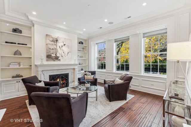 living room with built in shelves, crown molding, dark wood-type flooring, and a premium fireplace