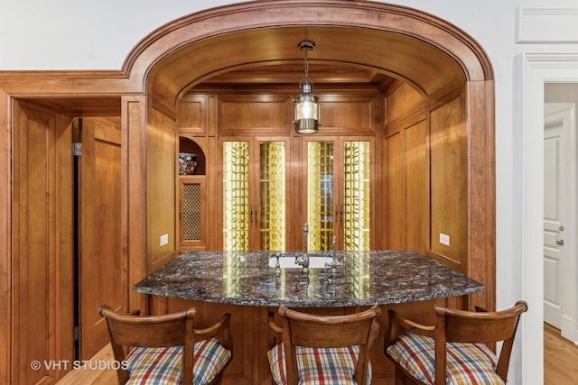 bar featuring hanging light fixtures, light wood-style floors, arched walkways, and wood walls