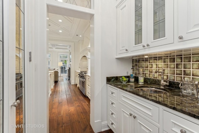 bar with stainless steel range, tasteful backsplash, dark wood-type flooring, a sink, and baseboards