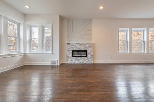 unfurnished living room with dark hardwood / wood-style flooring and a stone fireplace