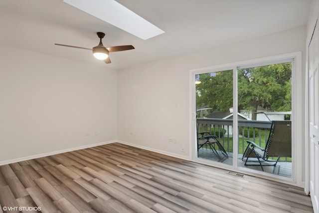 unfurnished room featuring a skylight, ceiling fan, and light wood-type flooring