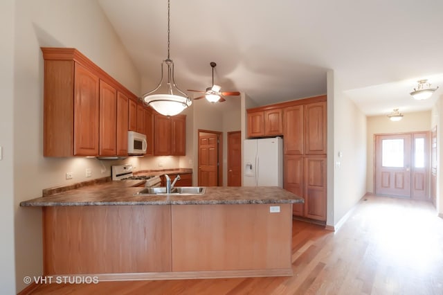 kitchen with white appliances, sink, hanging light fixtures, light hardwood / wood-style floors, and kitchen peninsula