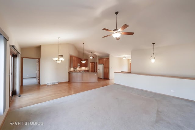 unfurnished living room with ceiling fan with notable chandelier, light wood-type flooring, and vaulted ceiling