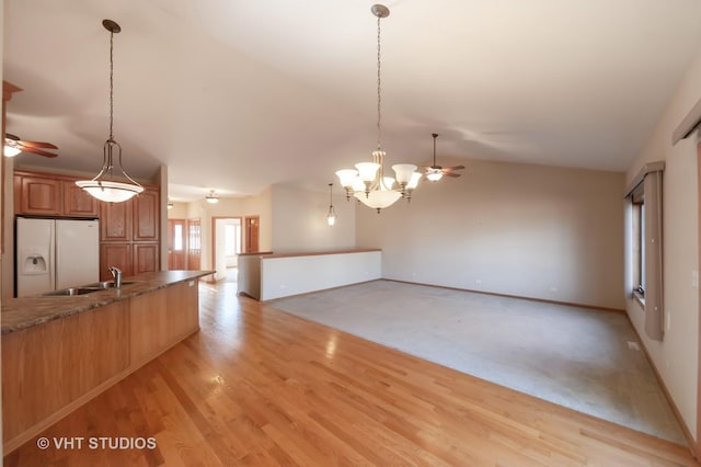 kitchen with sink, white refrigerator with ice dispenser, vaulted ceiling, decorative light fixtures, and light wood-type flooring