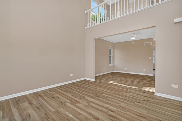 unfurnished living room with light wood-type flooring, a towering ceiling, and ceiling fan