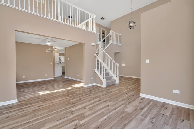 unfurnished living room with ceiling fan with notable chandelier, a towering ceiling, and light hardwood / wood-style flooring