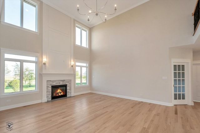 unfurnished living room with a stone fireplace, a towering ceiling, a healthy amount of sunlight, and light wood-type flooring