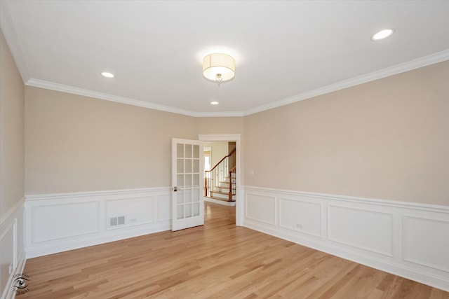 empty room featuring french doors, light wood-type flooring, and crown molding