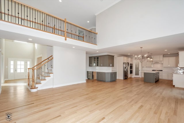 unfurnished living room featuring a notable chandelier, light hardwood / wood-style floors, and a high ceiling