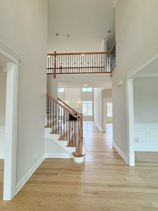 stairs with wood-type flooring, a towering ceiling, and crown molding