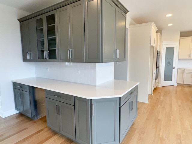 kitchen with backsplash, gray cabinets, double oven, and light wood-type flooring