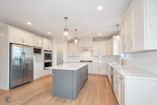 kitchen with a center island, hanging light fixtures, appliances with stainless steel finishes, light hardwood / wood-style floors, and white cabinetry