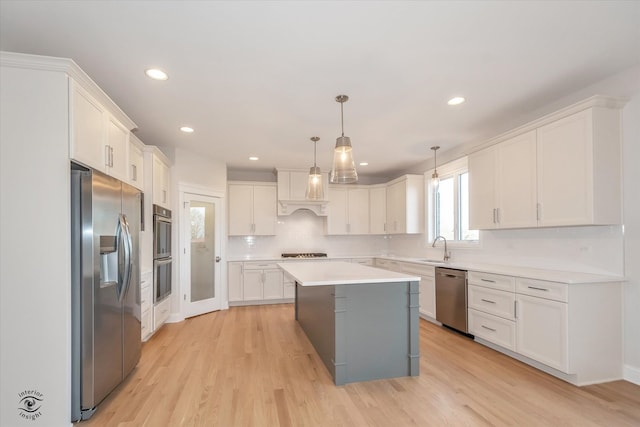 kitchen with white cabinetry, stainless steel appliances, pendant lighting, a kitchen island, and light wood-type flooring