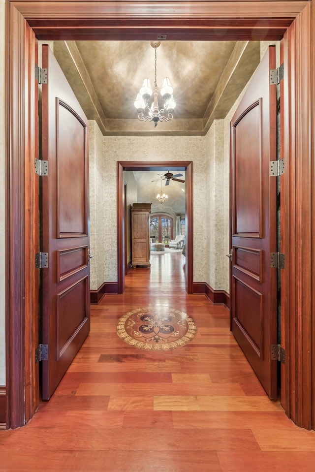 hallway with wood-type flooring, ornamental molding, and a notable chandelier