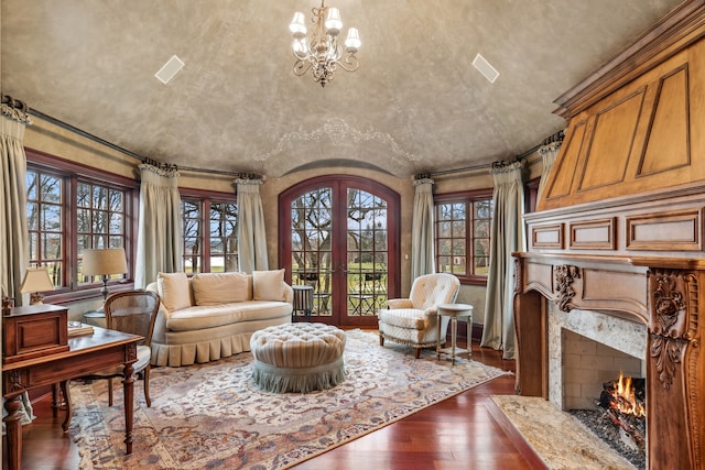 sitting room featuring a high end fireplace, french doors, vaulted ceiling, dark hardwood / wood-style flooring, and a chandelier