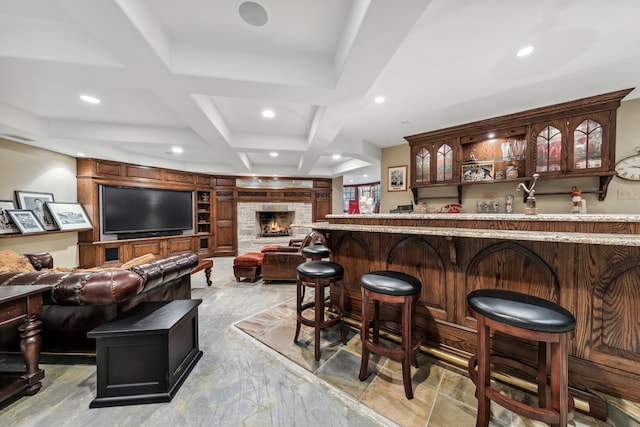 bar with beam ceiling, a stone fireplace, and coffered ceiling