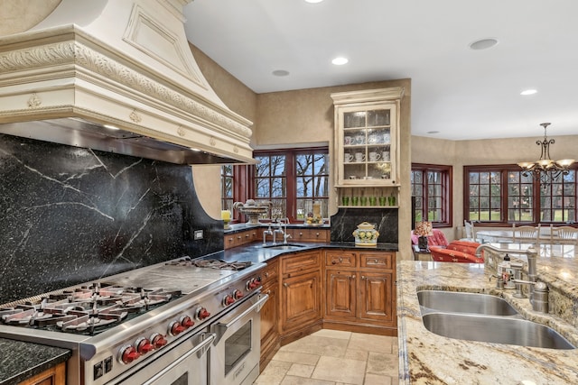 kitchen featuring custom exhaust hood, sink, stainless steel stove, decorative backsplash, and dark stone countertops