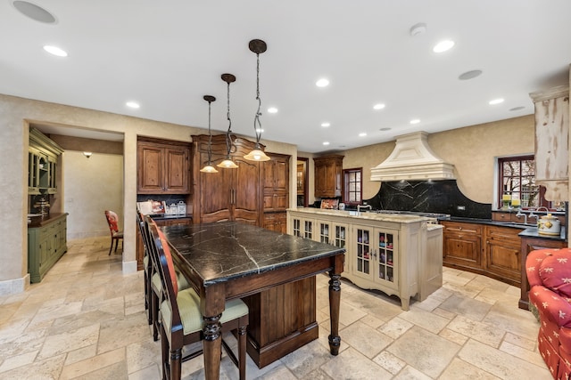 kitchen featuring hanging light fixtures, a spacious island, a breakfast bar area, decorative backsplash, and custom range hood