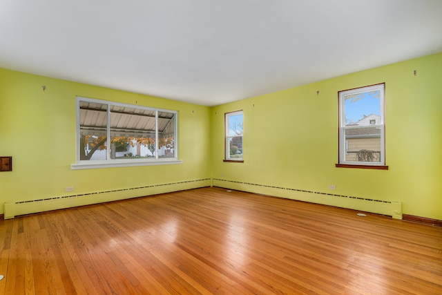 empty room featuring light wood-type flooring, baseboard heating, and plenty of natural light