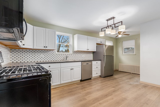 kitchen with light wood-type flooring, stainless steel appliances, white cabinetry, and radiator