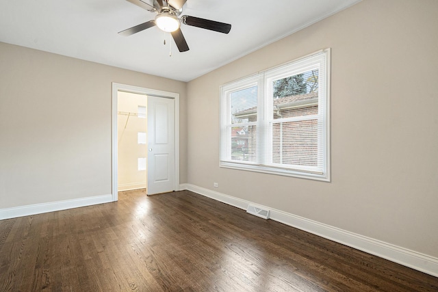 unfurnished bedroom featuring a spacious closet, dark wood-type flooring, ceiling fan, and a closet