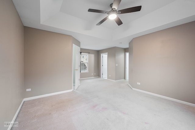 carpeted spare room with a raised ceiling and ceiling fan