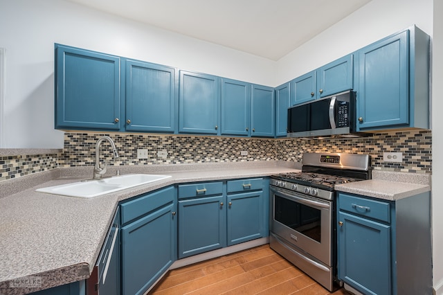 kitchen with decorative backsplash, appliances with stainless steel finishes, blue cabinets, sink, and light hardwood / wood-style flooring