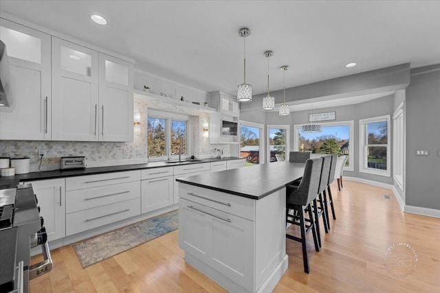 kitchen with white cabinetry, hanging light fixtures, tasteful backsplash, a kitchen breakfast bar, and a kitchen island