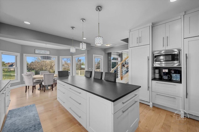 kitchen with pendant lighting, stainless steel microwave, white cabinetry, and light hardwood / wood-style flooring