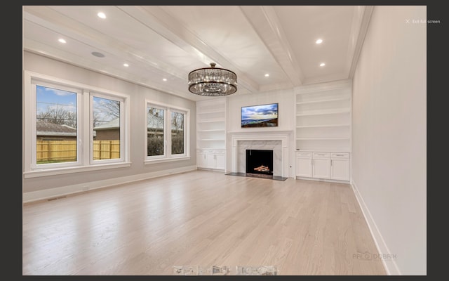 unfurnished living room featuring a high end fireplace, beam ceiling, light hardwood / wood-style flooring, built in features, and a notable chandelier