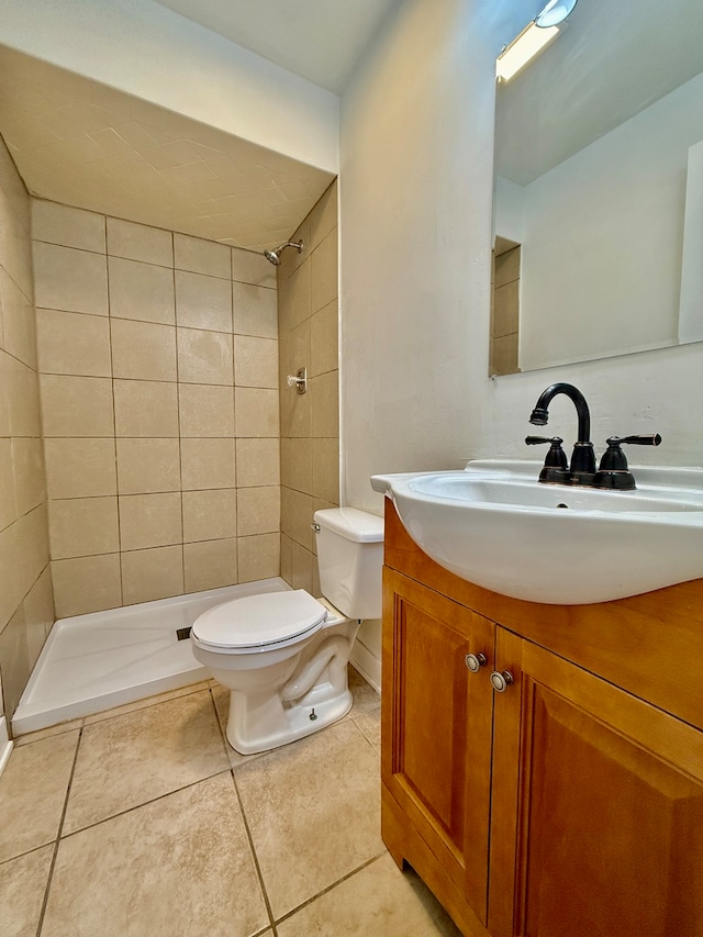 bathroom with tiled shower, tile patterned flooring, vanity, and toilet