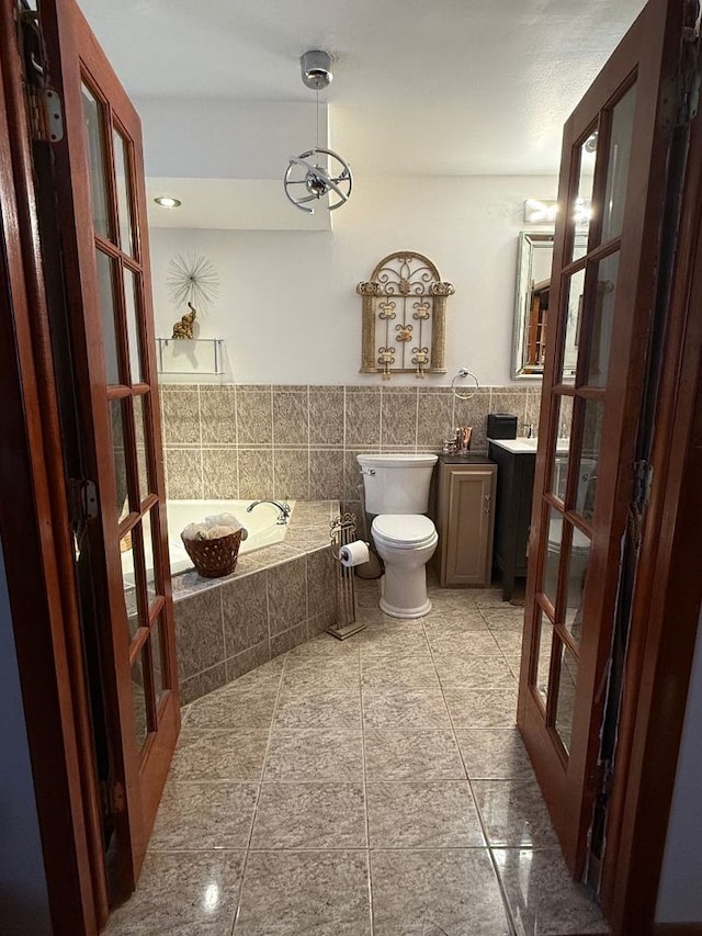 bathroom with vanity, toilet, tiled tub, and french doors