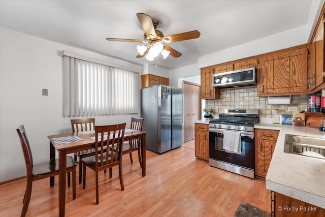 kitchen with decorative backsplash, appliances with stainless steel finishes, ceiling fan, sink, and light hardwood / wood-style flooring