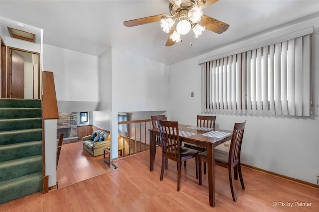 dining space featuring light hardwood / wood-style flooring, ceiling fan, and a stone fireplace