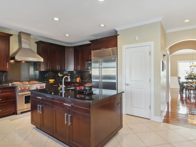 kitchen featuring sink, wall chimney exhaust hood, a kitchen island with sink, light tile patterned floors, and high end appliances