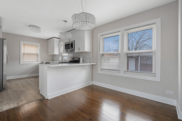 kitchen with pendant lighting, white cabinets, appliances with stainless steel finishes, tasteful backsplash, and kitchen peninsula