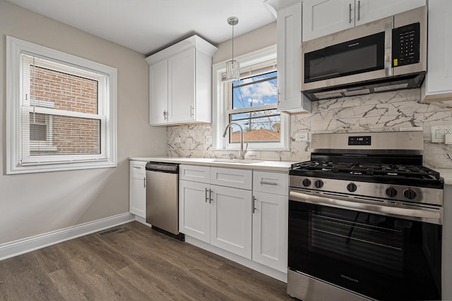 kitchen with appliances with stainless steel finishes, dark hardwood / wood-style flooring, tasteful backsplash, decorative light fixtures, and white cabinetry